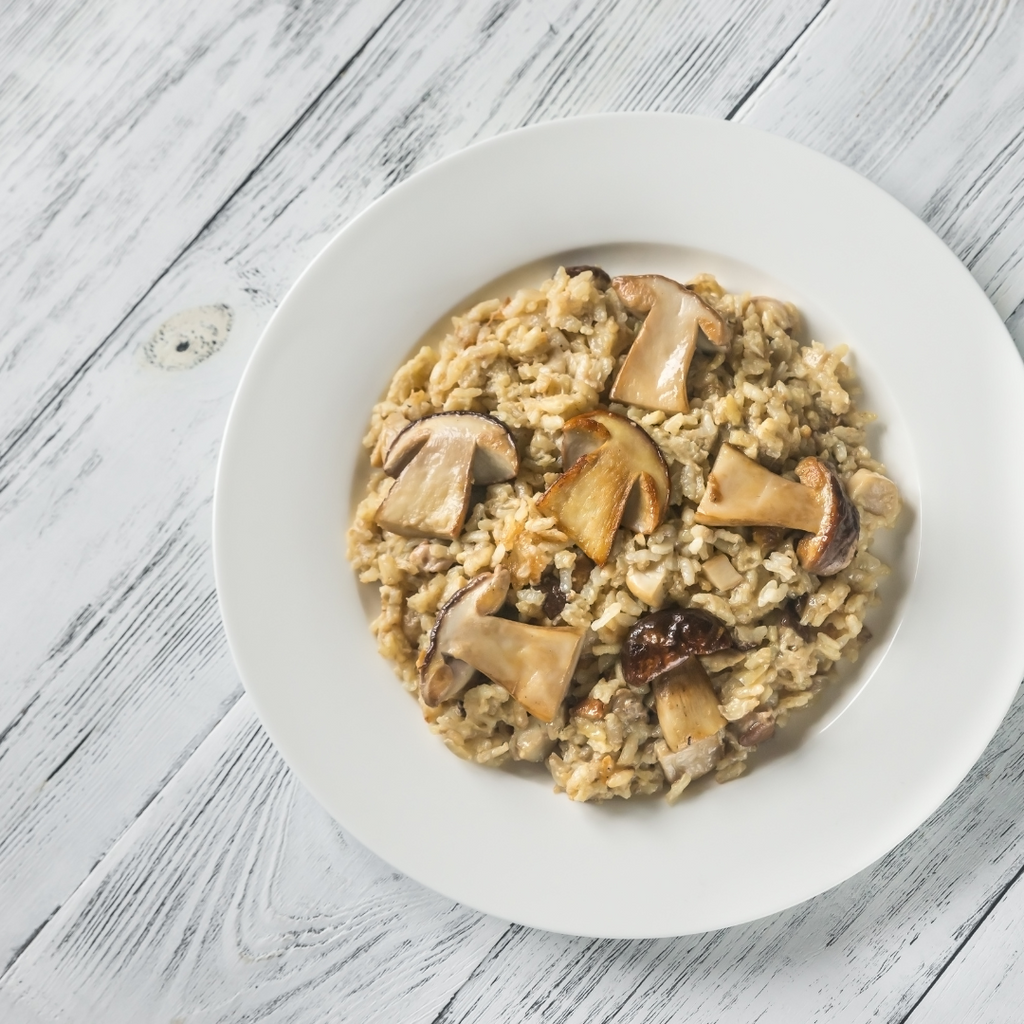 A top-down view of a white plate containing a mushroom-infused rice dish, set on a white-washed wooden table.