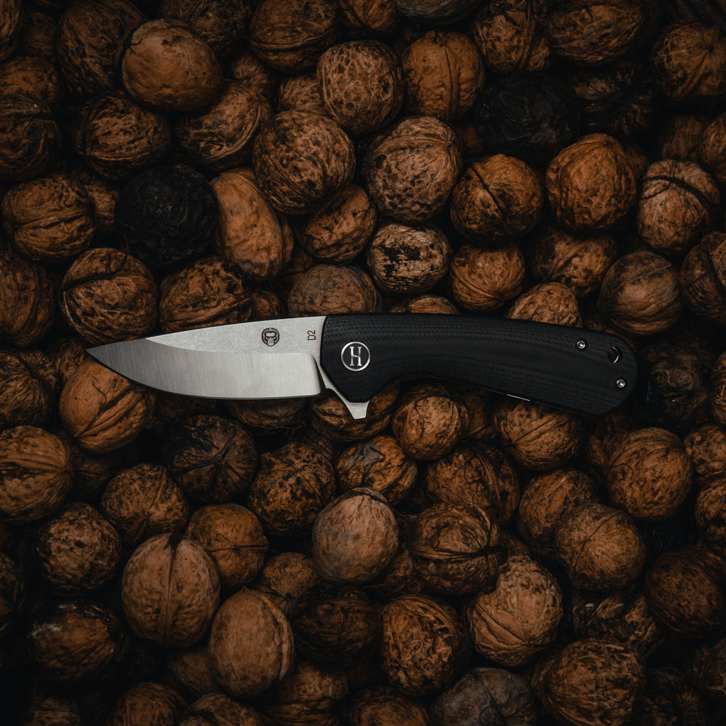 Knife with a black handle and silver blade on a pile of walnuts