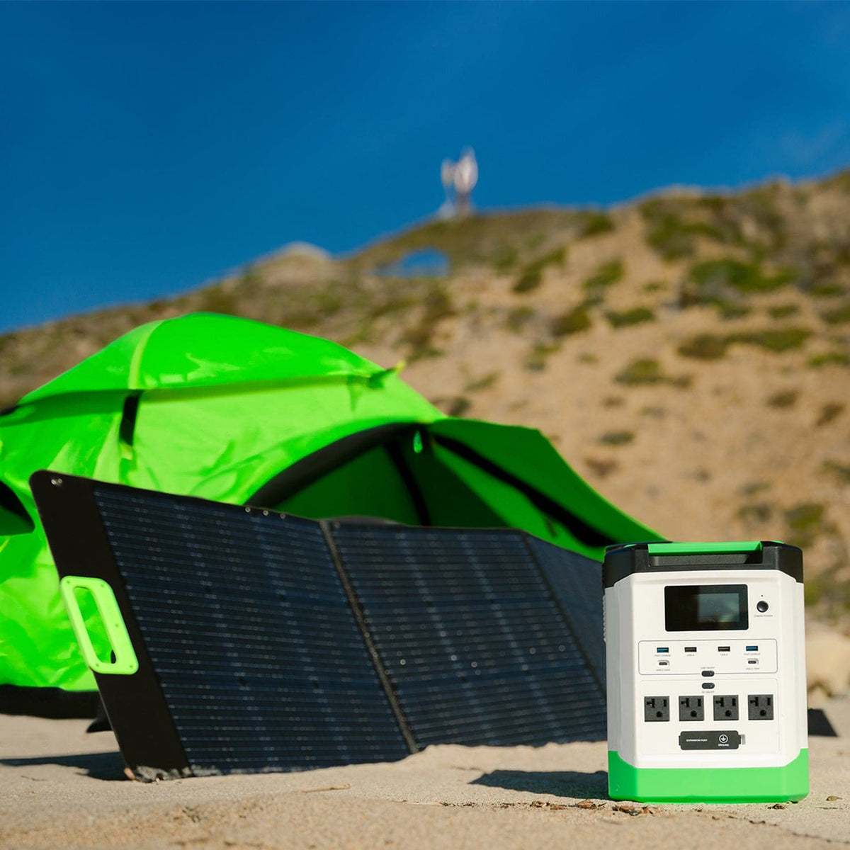 Solar panel and power station in front of a green tent on a camping site with a mountain in the background.