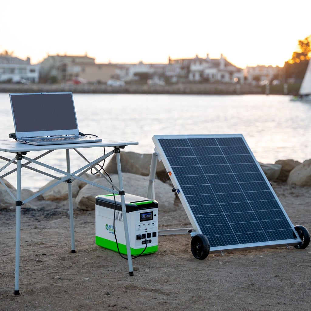 Solar panel, portable power station, and laptop on a beach with a scenic background.