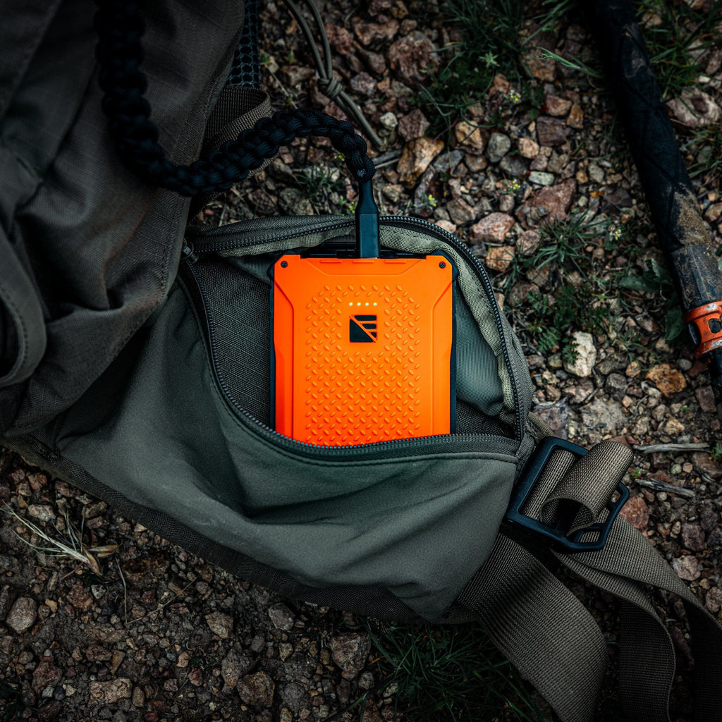 Orange power bank in a green backpack on a rocky ground