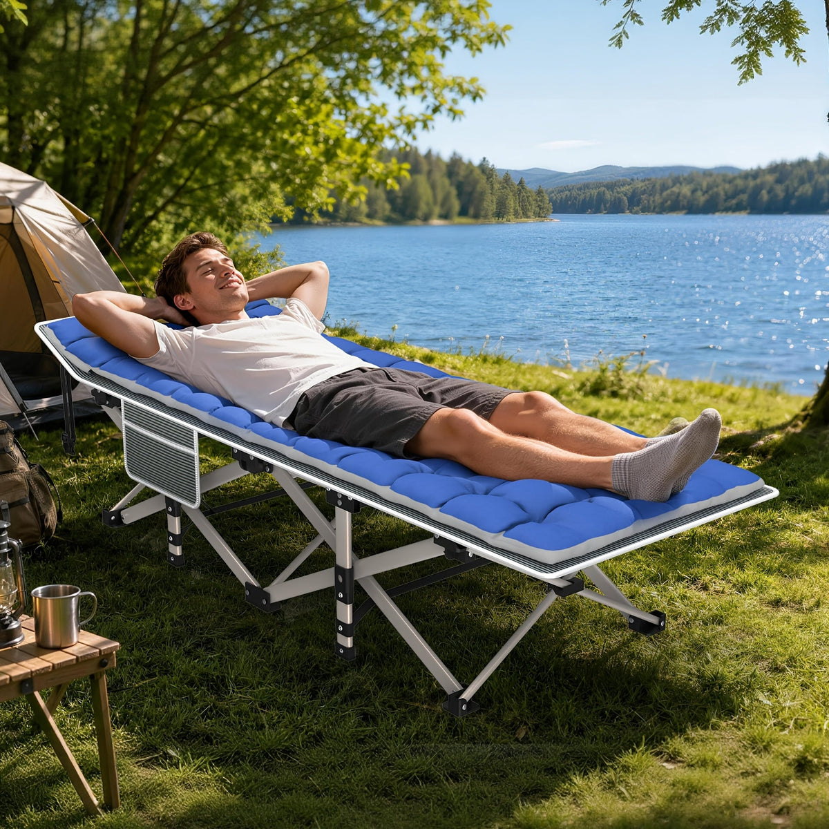 Person relaxing on a camping cot by a lake with a tent in the background