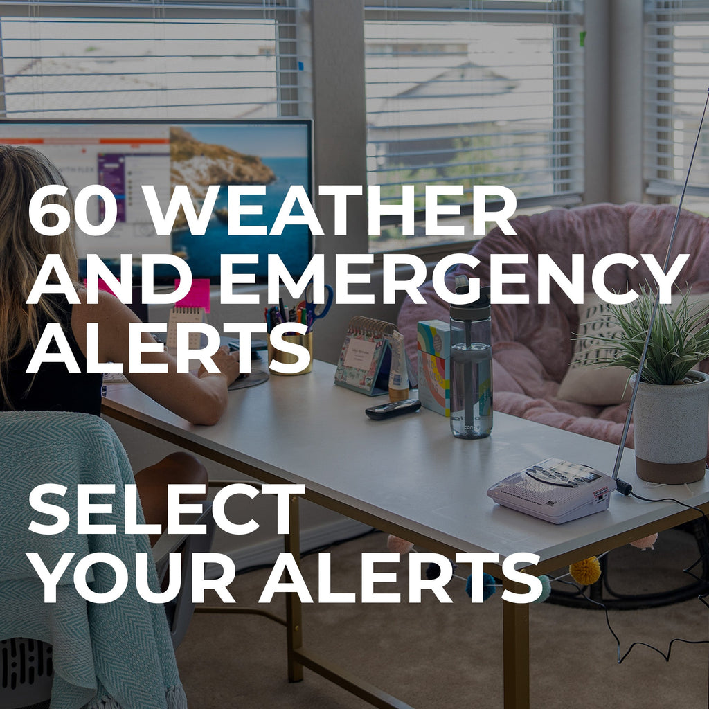 A woman sits at a desk in a home office or living space, with large overlaid text reading '60 WEATHER AND EMERGENCY ALERTS' and 'SELECT YOUR ALERTS'. The room includes a monitor, table, water bottle, small plant, and couch in the background.
