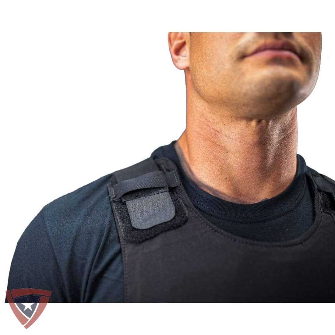 Close-up of a man wearing a black tactical vest over a dark crewneck shirt, showing the shoulder strap and chest panel of the vest against a white background.
