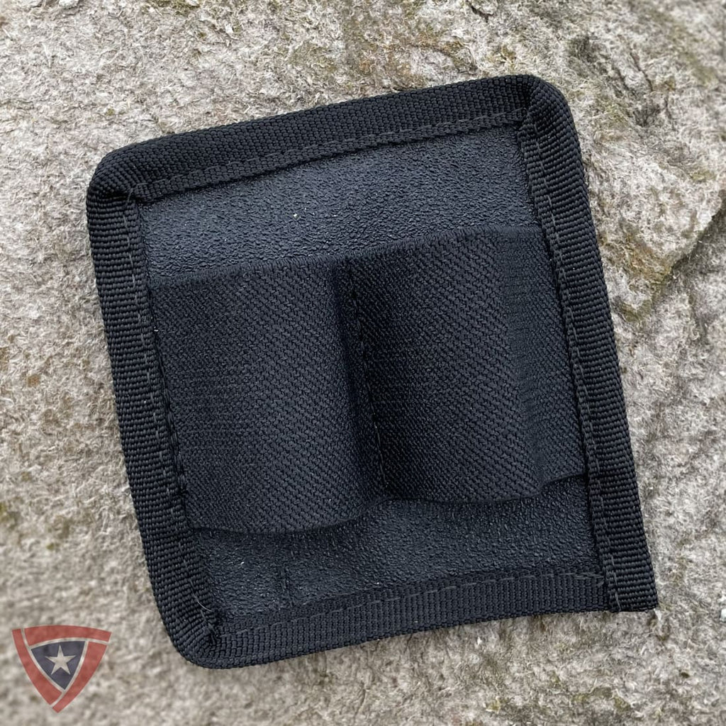 A black nylon dual-bottle holder patch with a stitched border, shown on a textured gray stone background.