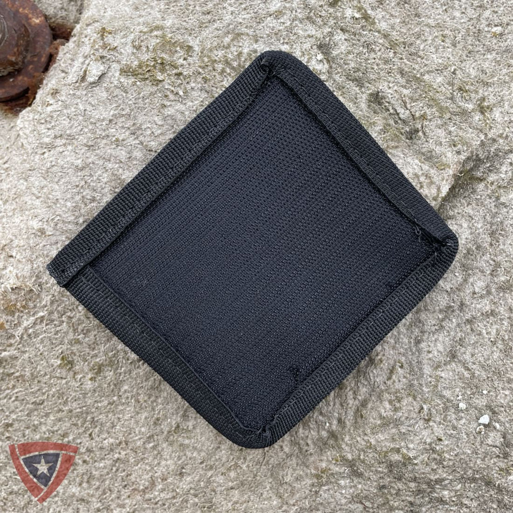 A black textured fabric pouch or wallet with reinforced stitched edges, photographed from above on a rough light gray stone surface.