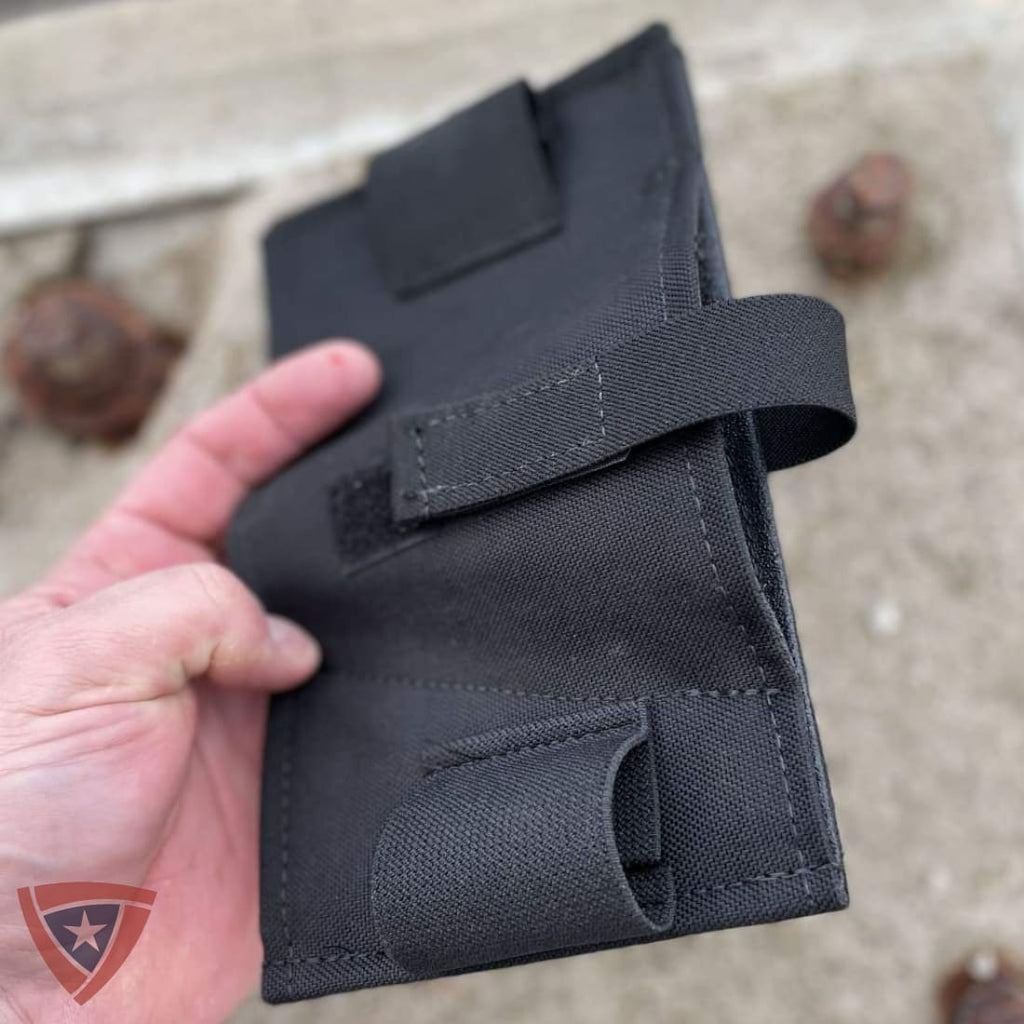A black tactical pouch or holster made of durable fabric, held in a hand against a sandy outdoor background.