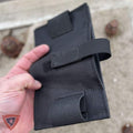 A black tactical pouch or holster made of durable fabric, held in a hand against a sandy outdoor background.