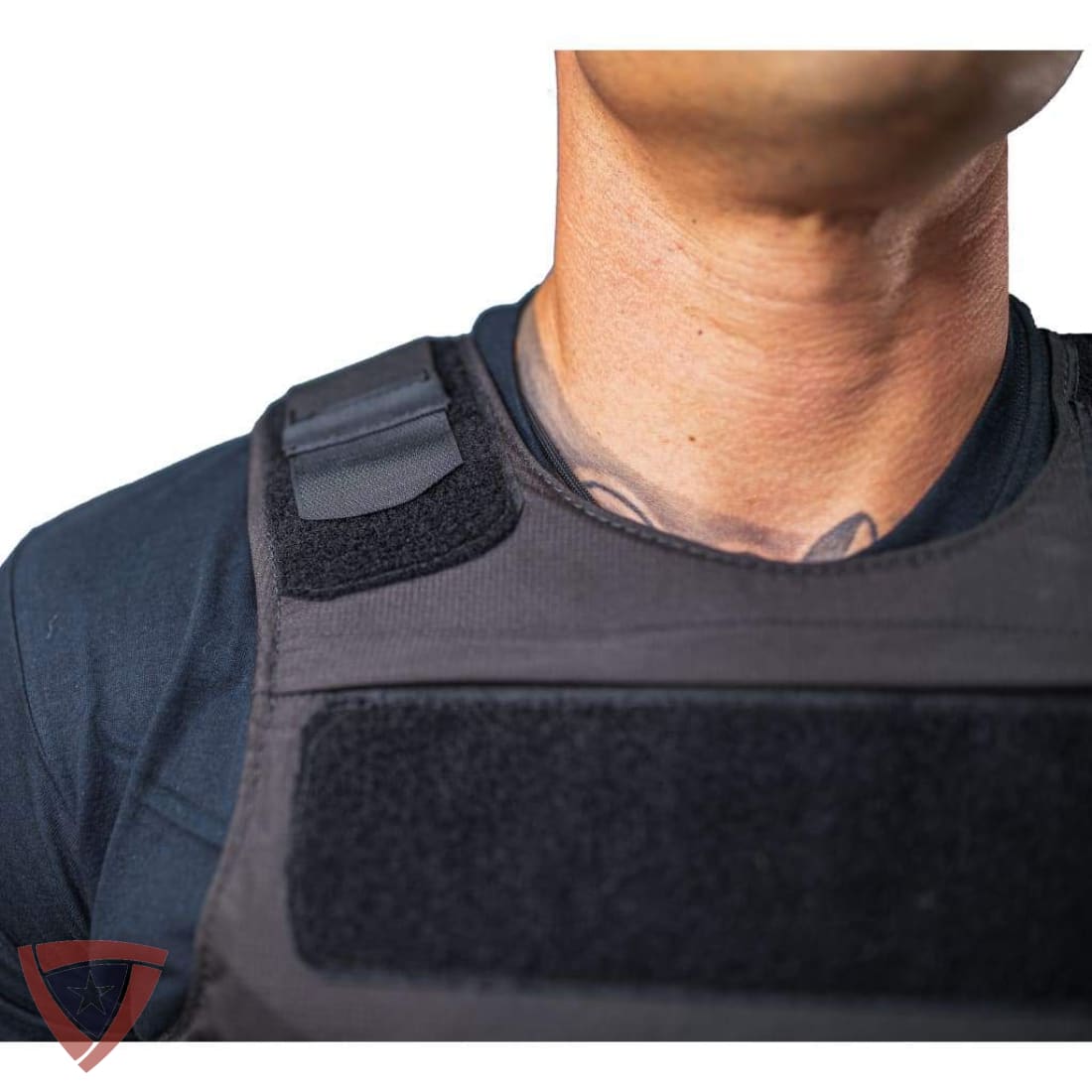 Close-up of a person wearing a black tactical vest over a dark shirt, showing the collar area and shoulder strap details against a white background.