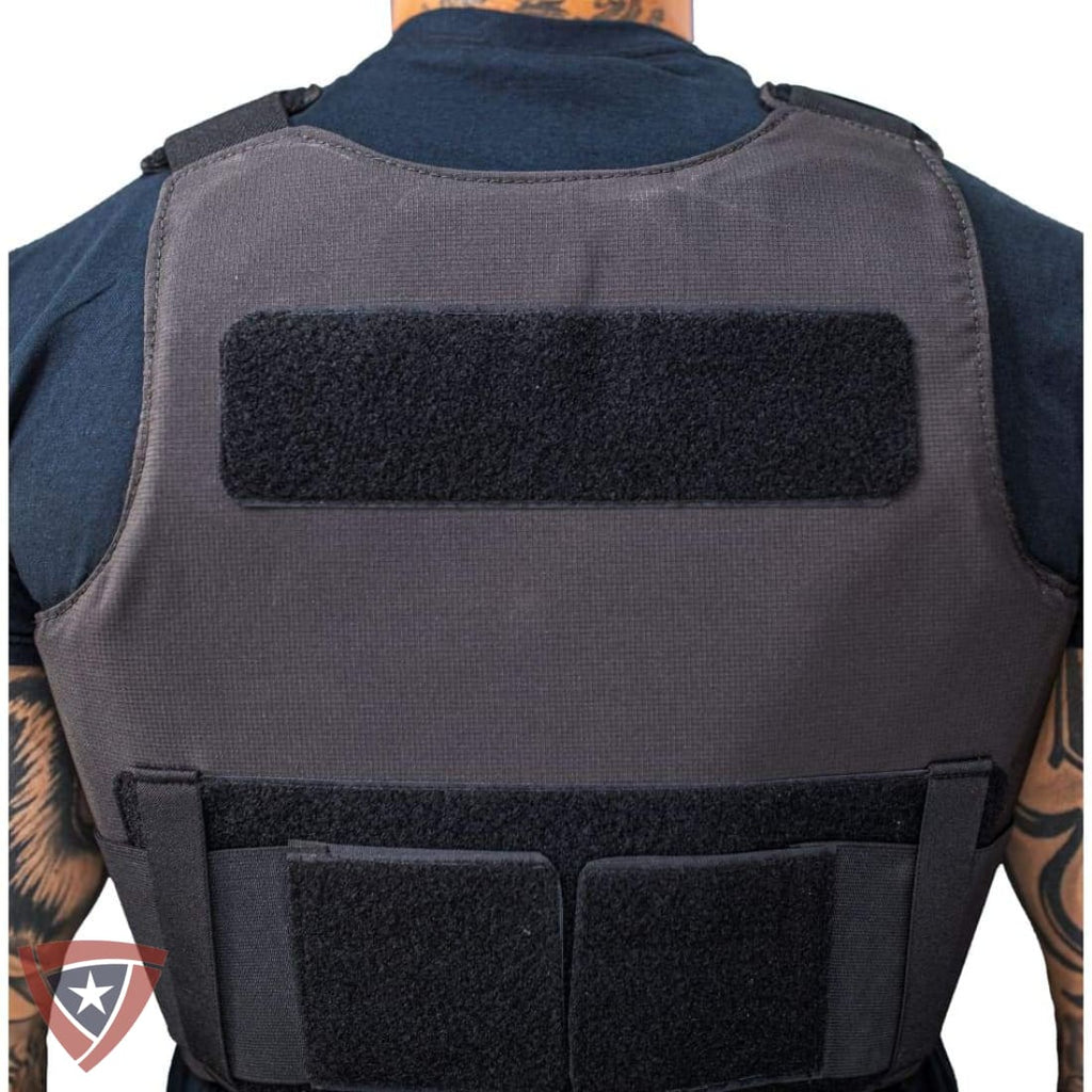 A dark gray tactical vest with black velcro patches, shown from the back on a model wearing a navy blue shirt. The vest features a horizontal velcro strip on the upper back and two vertical velcro pockets on the lower back.