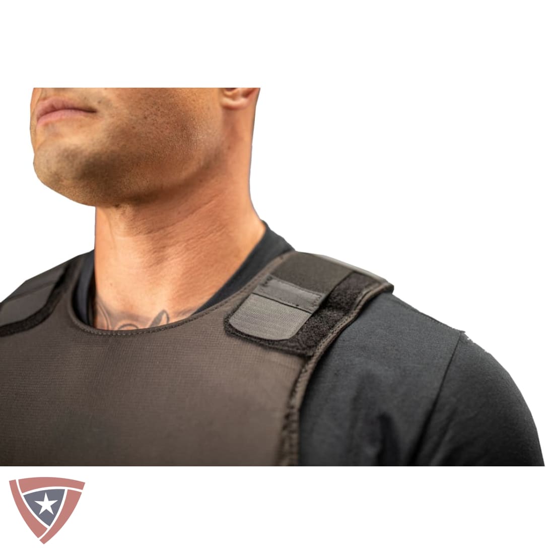 Close-up of a man wearing a black tactical vest over a black shirt, showing the shoulder strap and chest panel, on a white background with a logo in the bottom-left corner.
