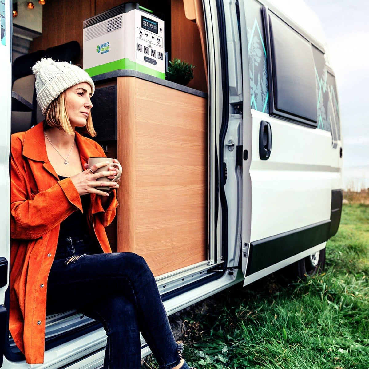 Woman sitting inside a van with a portable power station, holding a mug.